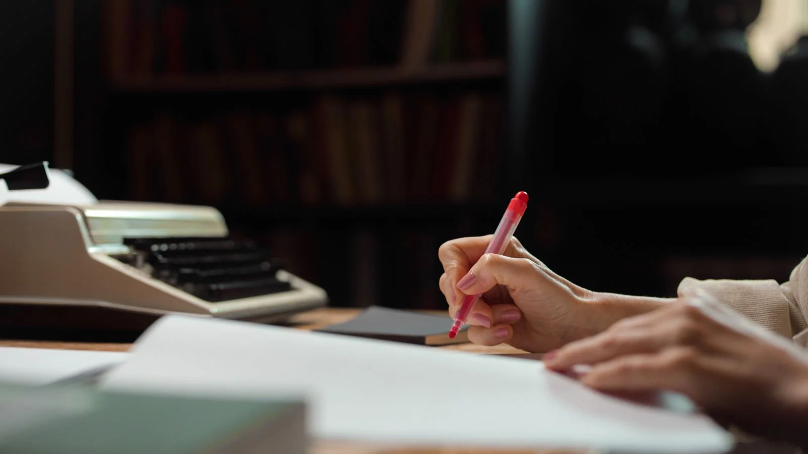 Hand writing with a pen in a library beside a vintage typewriter, logging evidence before applying