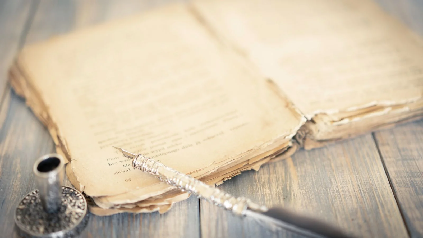 Antique book and vintage pen resting on a rustic wooden table, the tools of a careful first draft