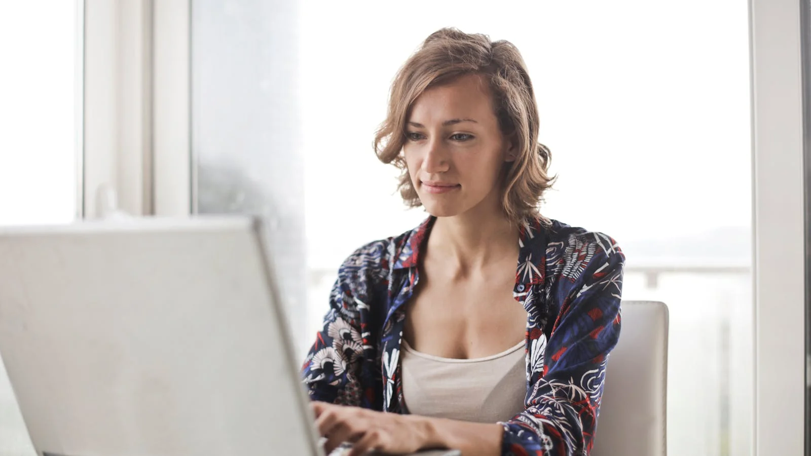 A person writing at a laptop in a bright home office