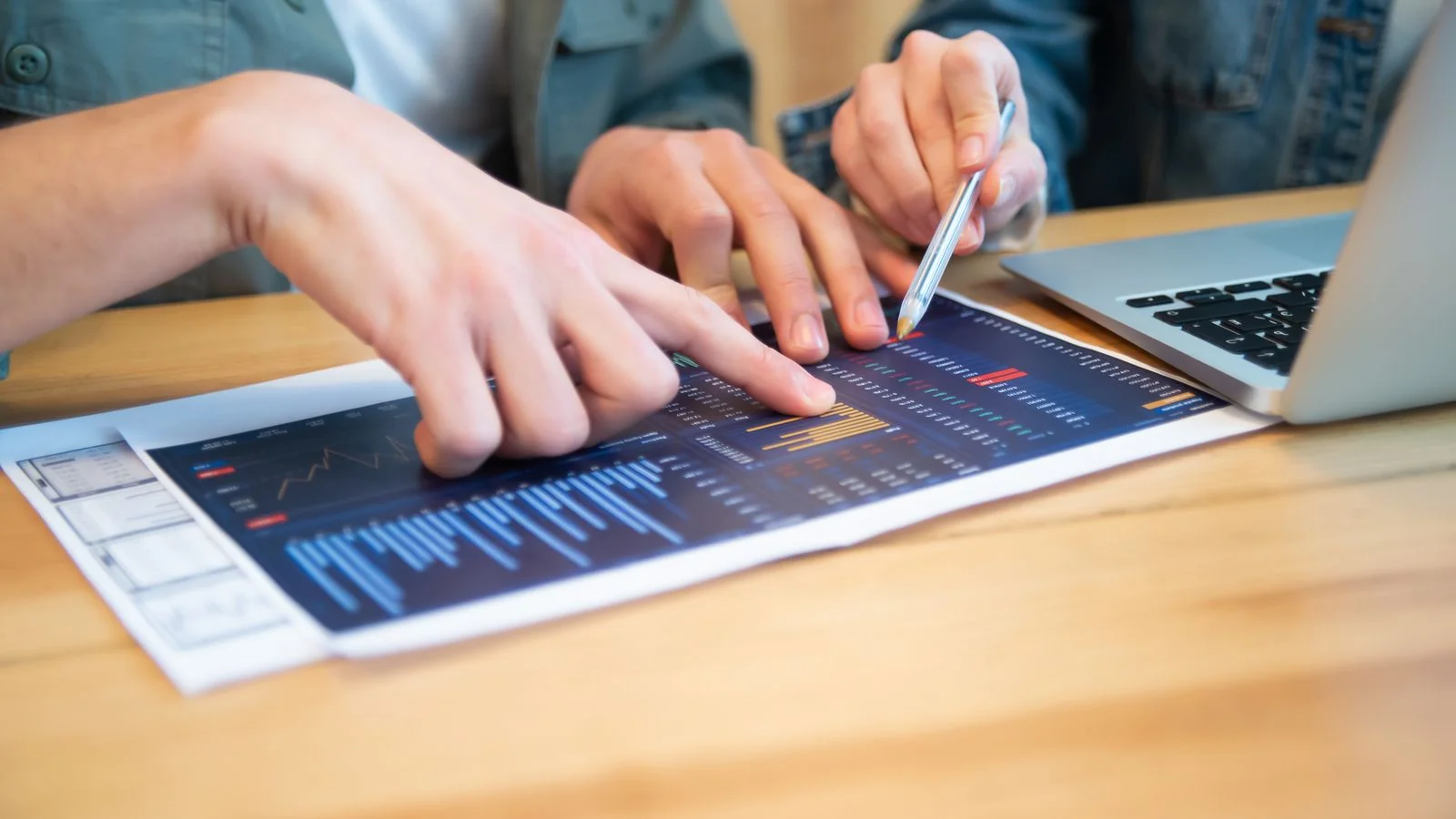 Two professionals discussing data charts over a laptop, testing an argument against its best objection