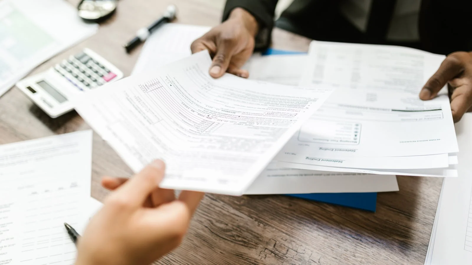 Two professionals exchanging printed documents across a table in an office