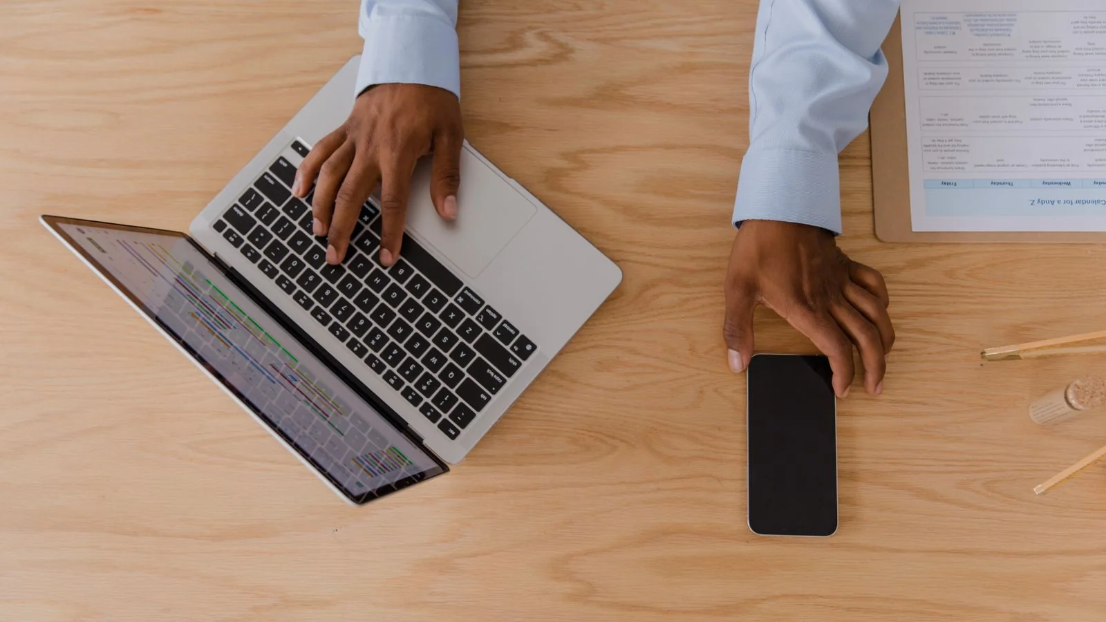 Hands using a laptop and smartphone on a wooden desk while sorting an email inbox