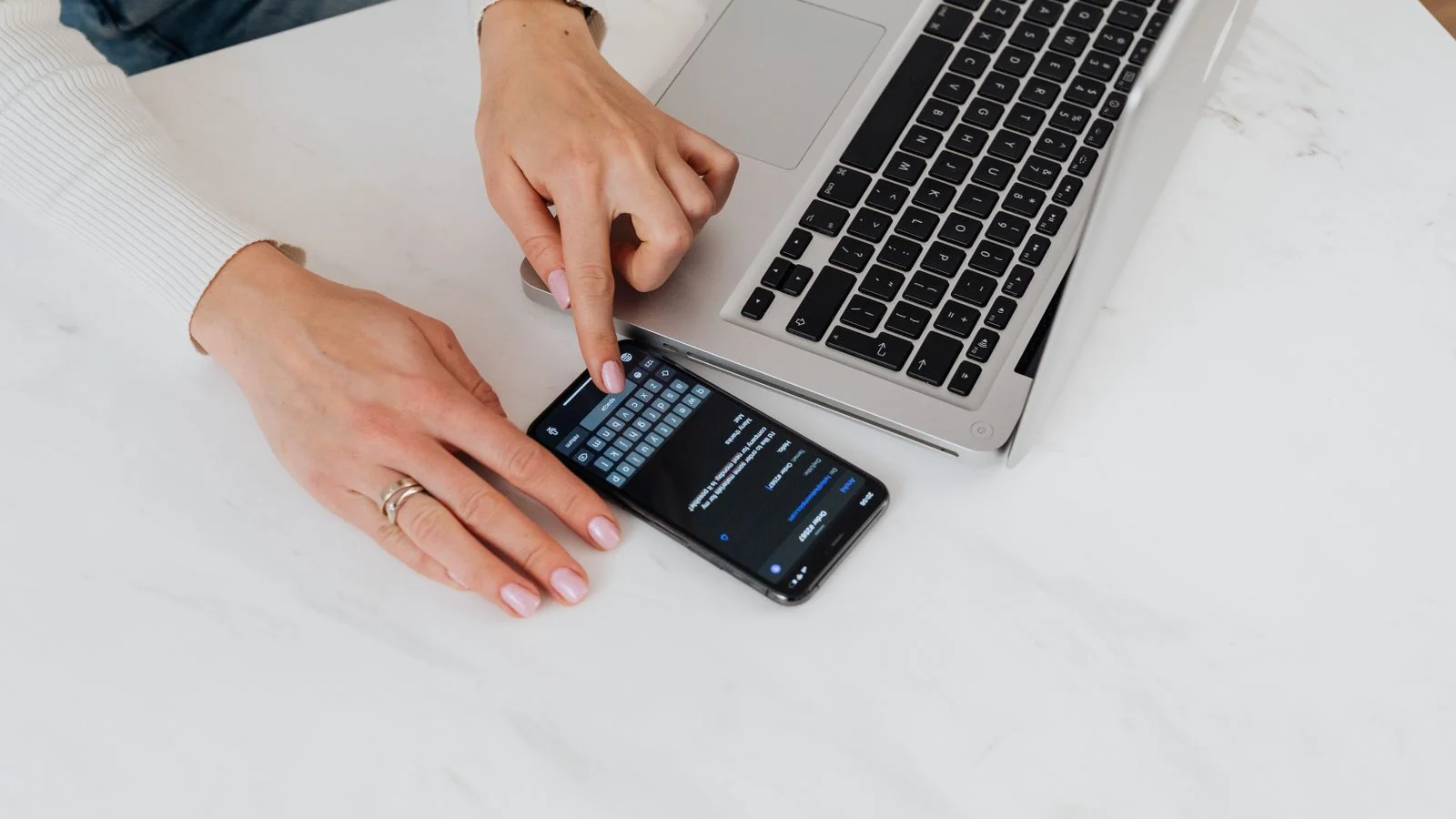 Smartphone and laptop side by side on a white desk, comparing personalized search results