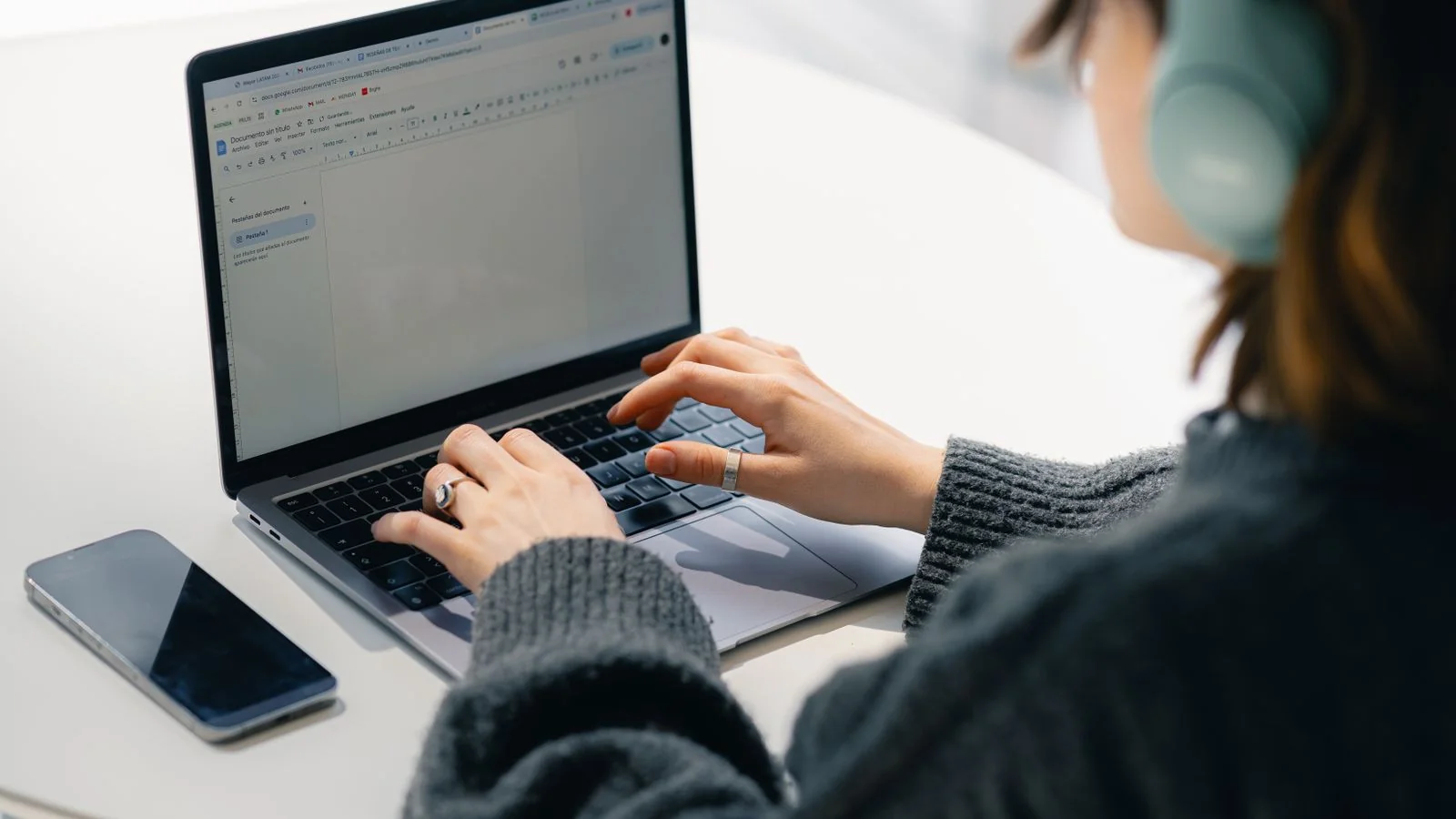 Woman with headphones typing outreach emails on a laptop at a white table