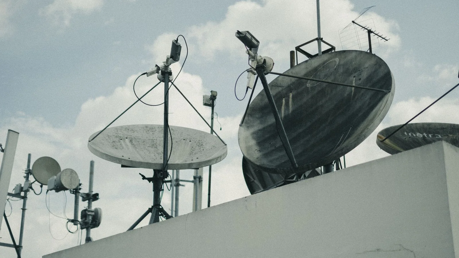 Satellite dishes and antennas on a rooftop under a cloudy sky, the infrastructure behind local broadcast news