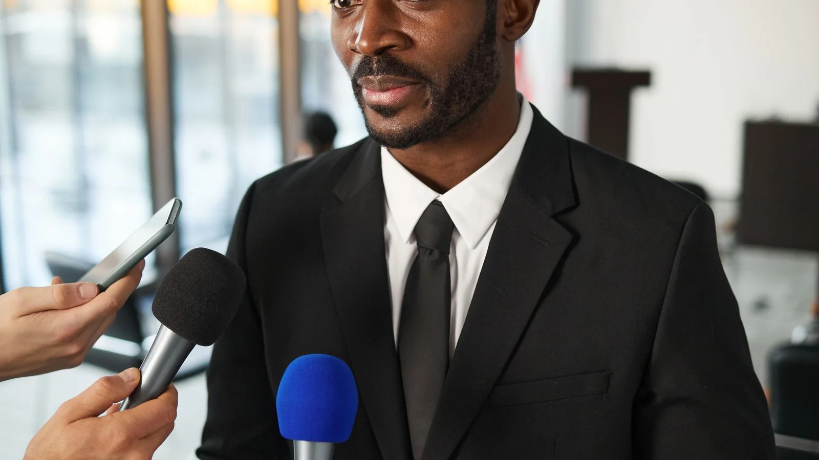 Reporters holding microphones toward a speaker at a scheduled event, the coverage an advisory is meant to produce