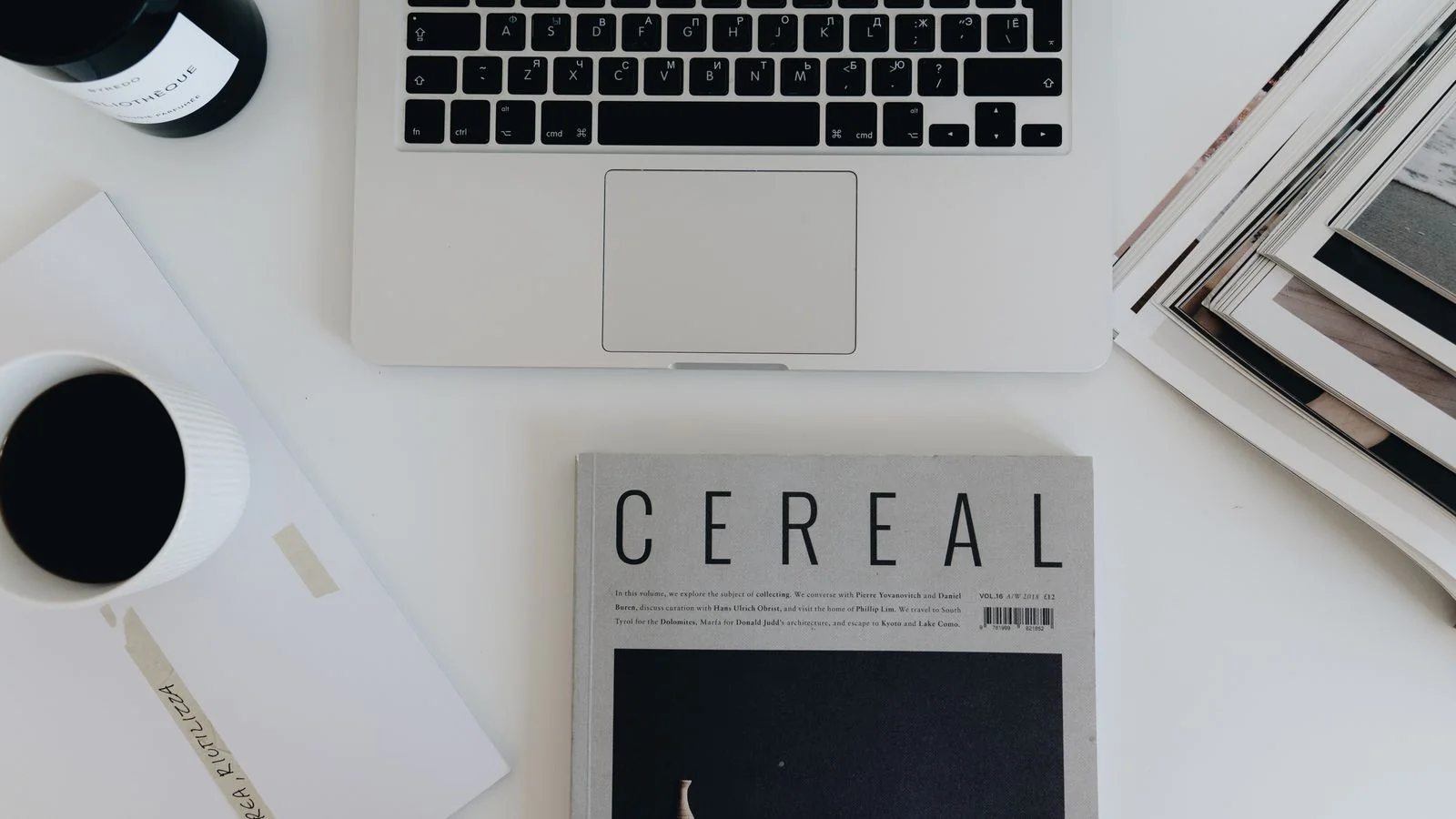 A flatlay of magazines, a laptop, and coffee, the mixed materials that inform editorial decisions