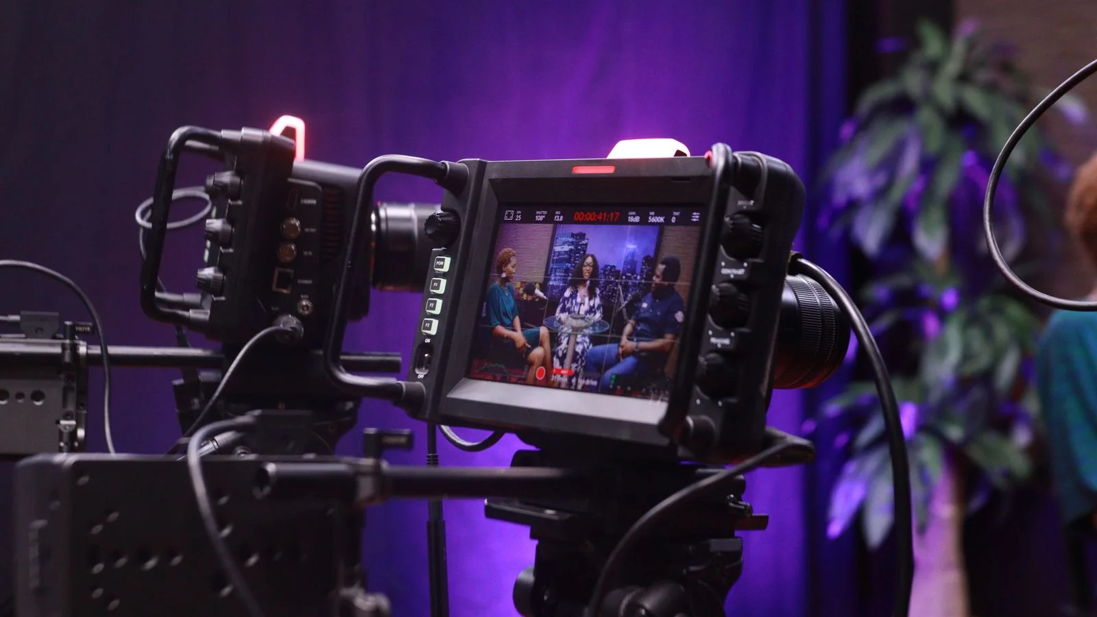 A professional video camera set up to record an interview, subject softly out of focus behind it