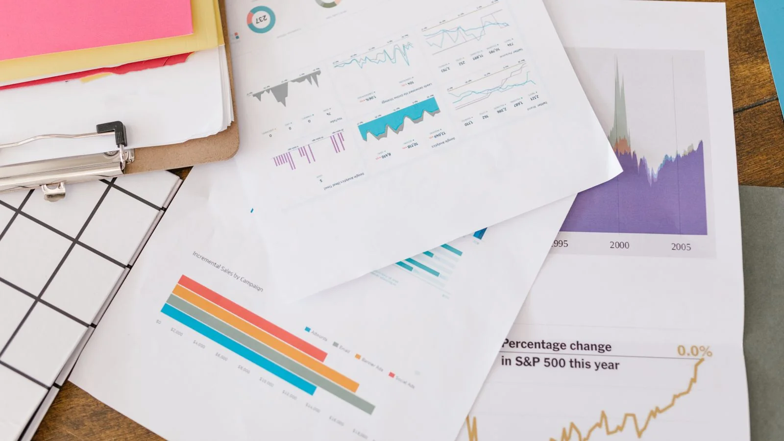 Business analytics charts and graphs spread across papers and a clipboard on a desk