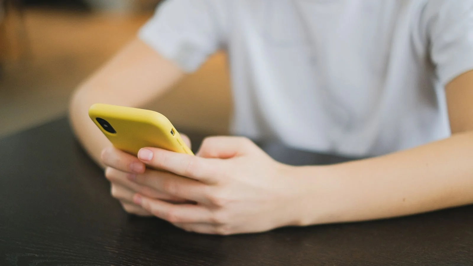 Close-up of hands holding a yellow smartphone indoors