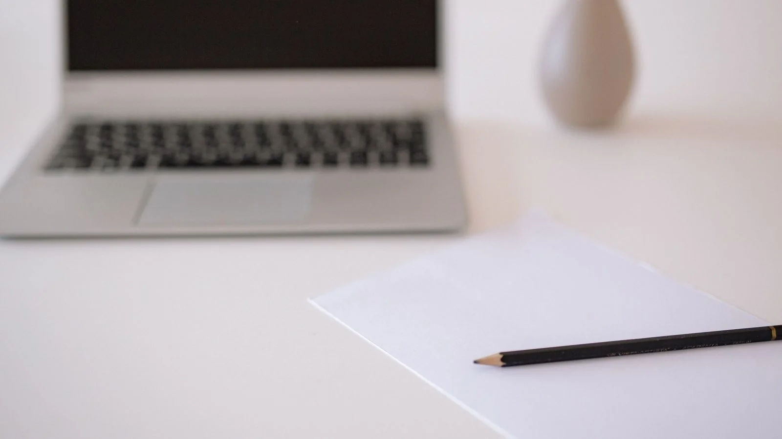 A person writing clear notes beside a laptop, drafting the plain factual statements an About page needs