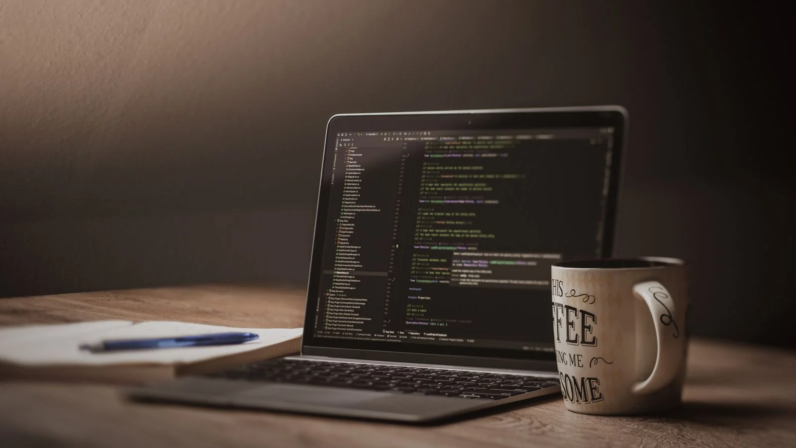 Laptop showing code beside a coffee mug and notepad, the setup for writing JSON-LD by hand