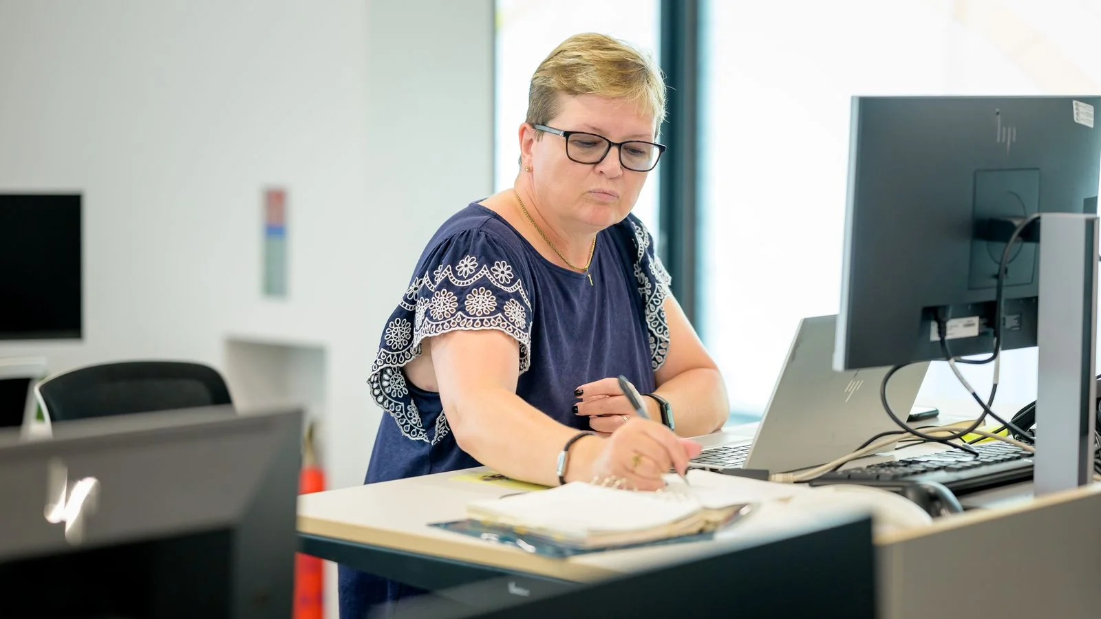 A person writing in a notebook beside a laptop, creating content for a brand's owned channels