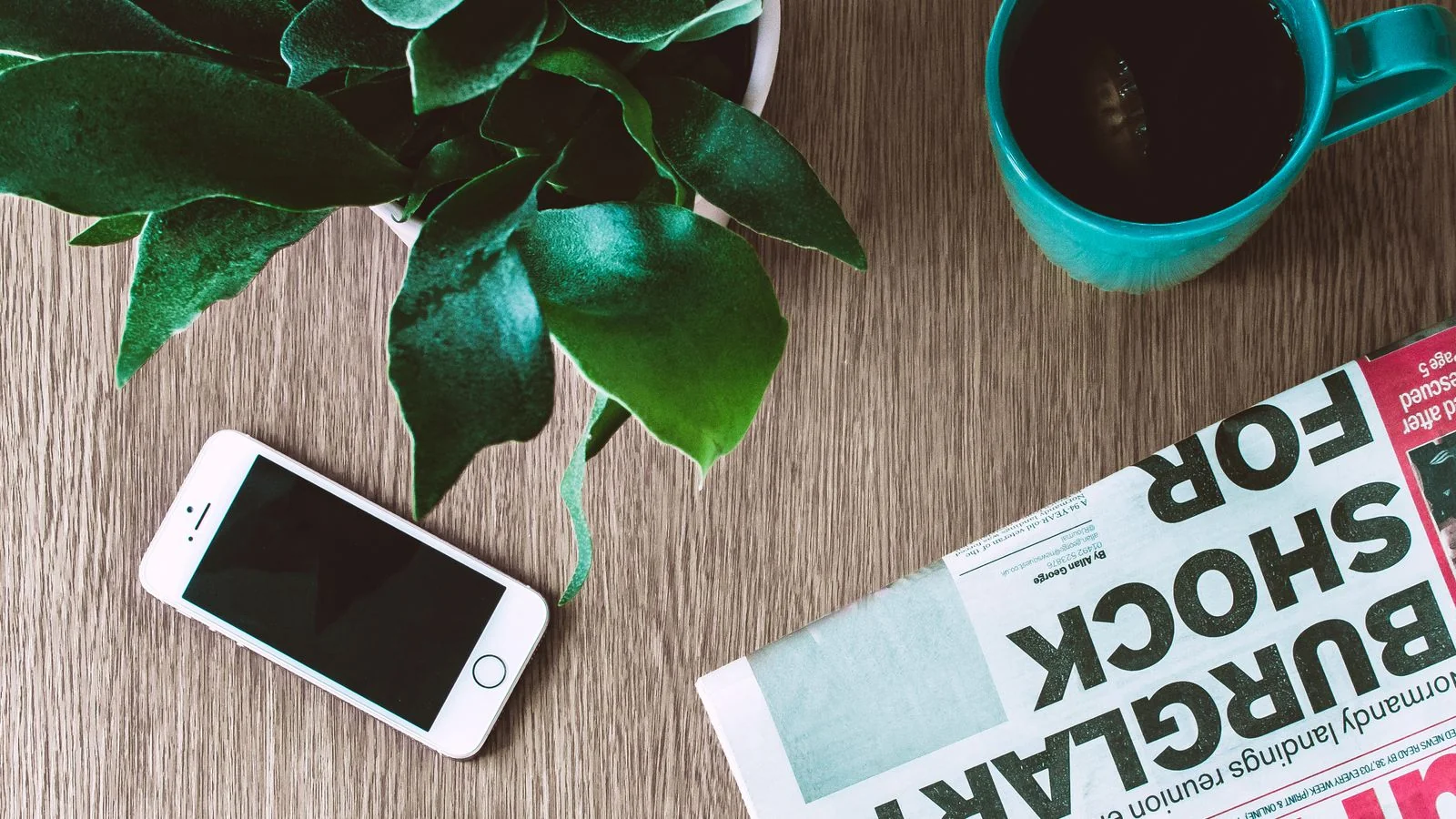A laptop with a phone and newspaper on a desk, the mix of owned channels a brand builds and keeps