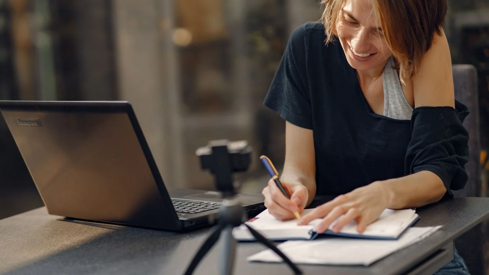 Woman smiling as she writes notes beside her laptop, budgeting a tool decision