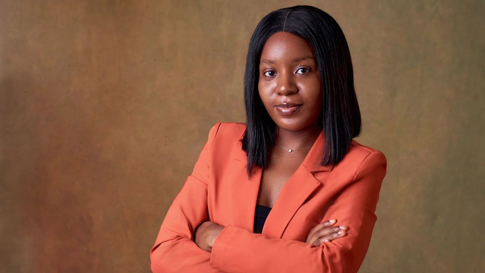 Confident woman in an orange blazer with arms crossed, a portrait of a defined personal brand