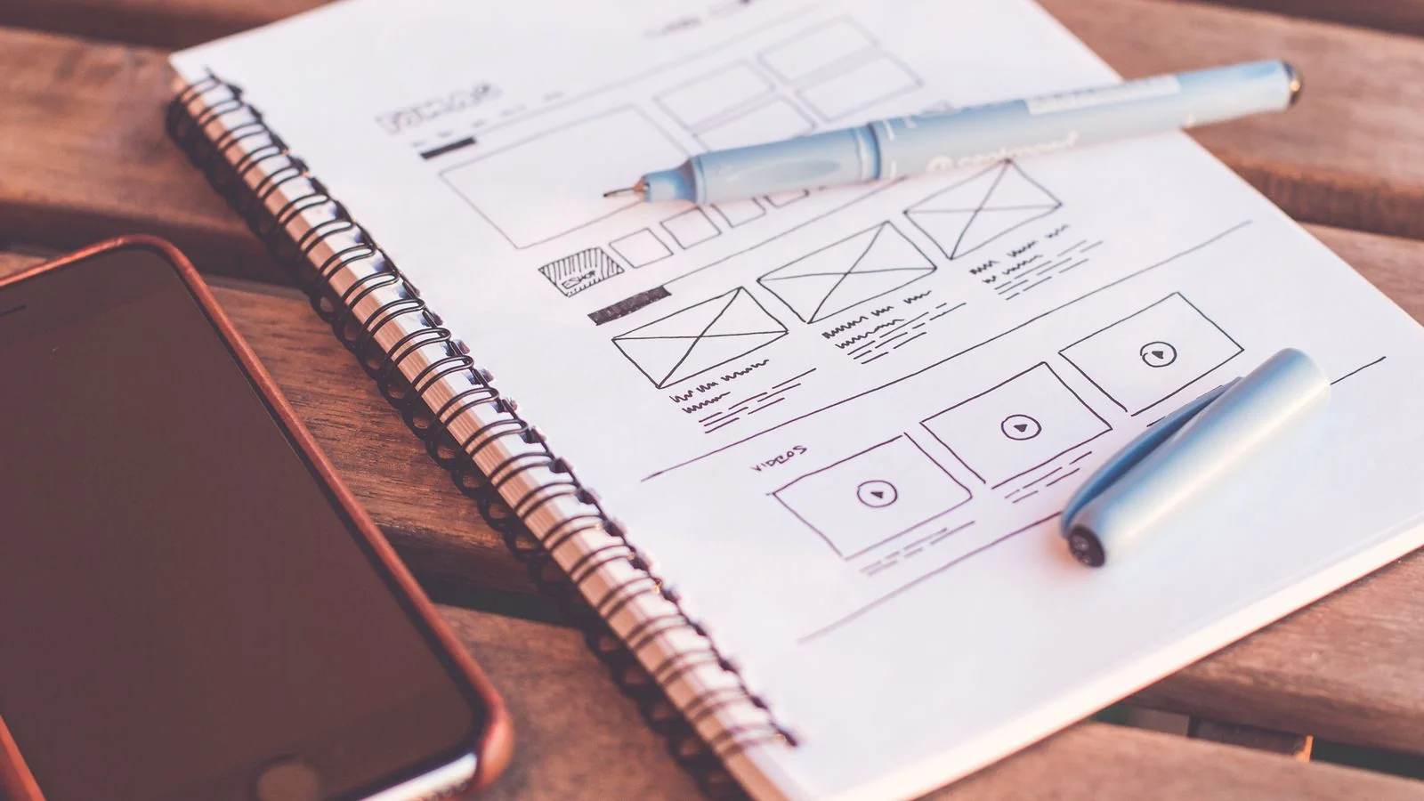 Hand-drawn wireframe sketches in a notebook beside a smartphone, the planning stage of a personal site