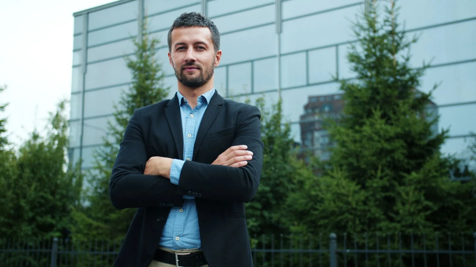 Businessman standing with arms crossed in front of a modern office building outdoors