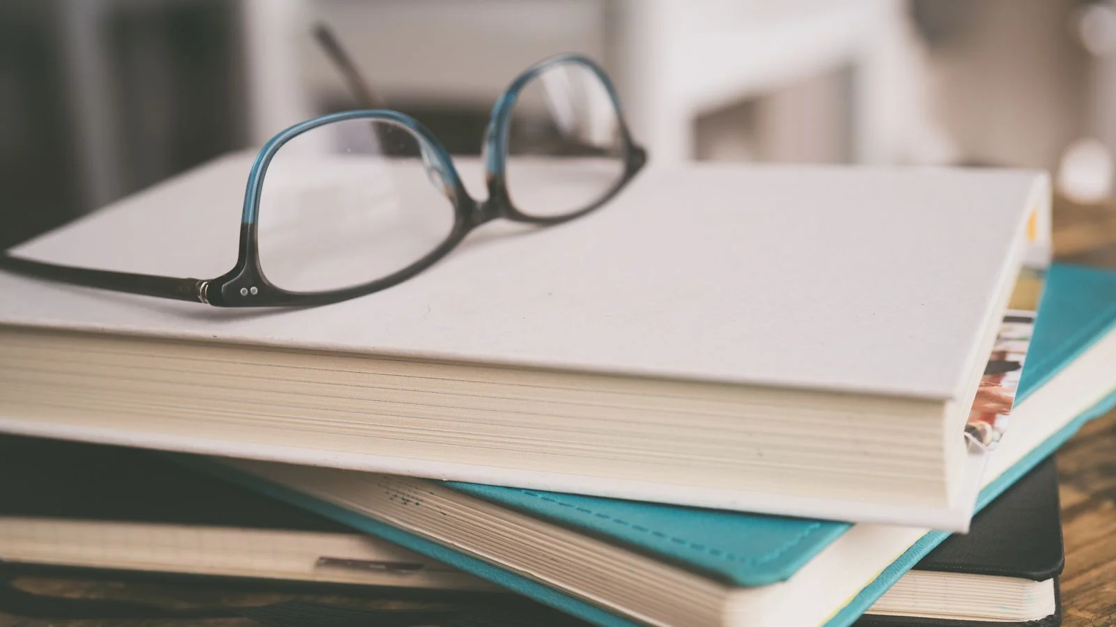 Black-framed eyeglasses resting on a stack of books in a quiet study setting