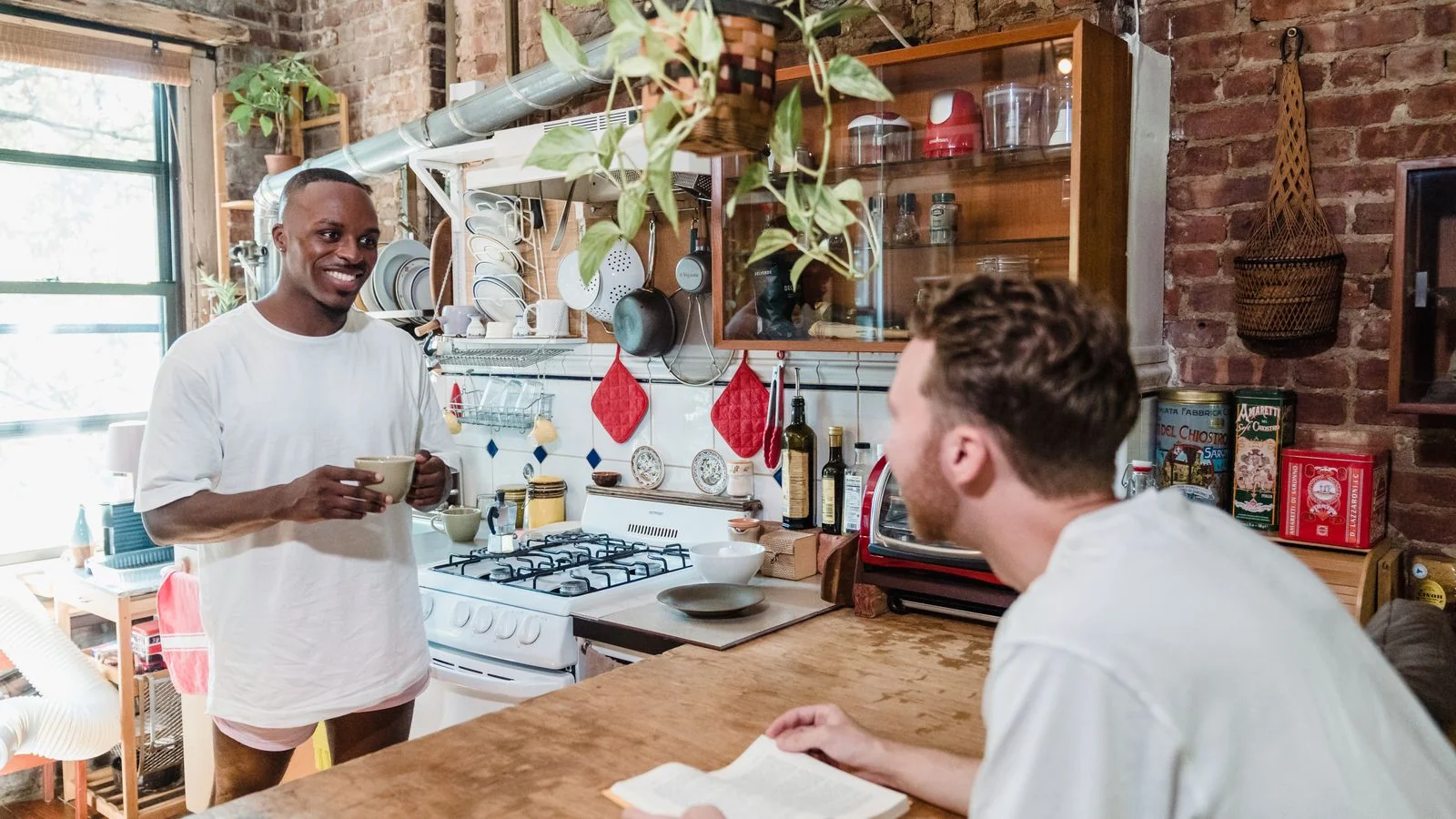 Two guests lingering over coffee and books in a rustic kitchen, the kind of morning a host designs rather than a building provides.
