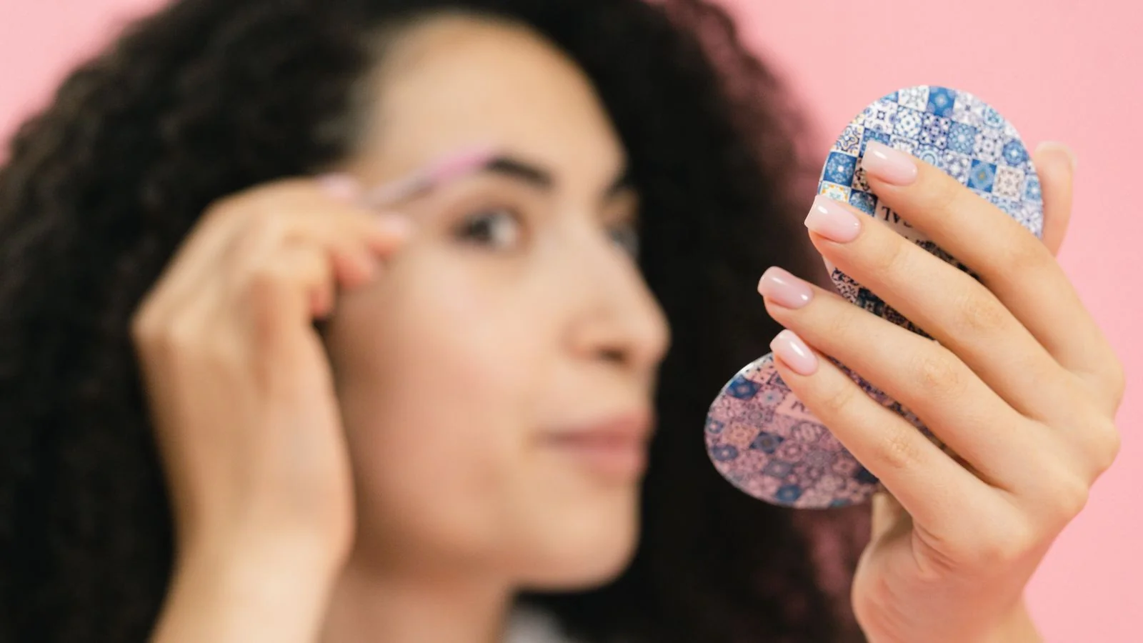 A woman checking her brows in a compact mirror, the private verdict every brow appointment is judged against