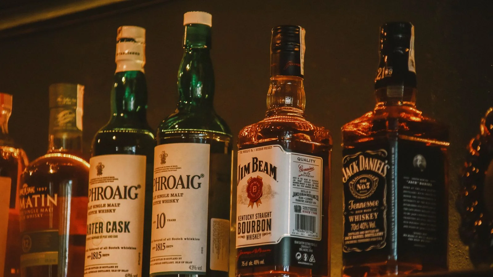 Whiskey bottles lined up on a backlit bar shelf.