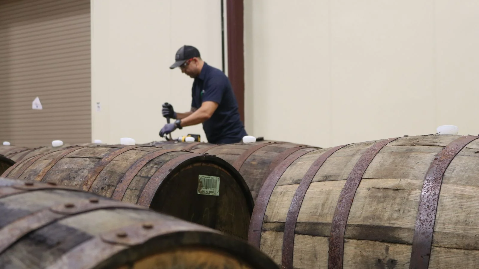 A worker inspecting barrels stacked in a rickhouse.