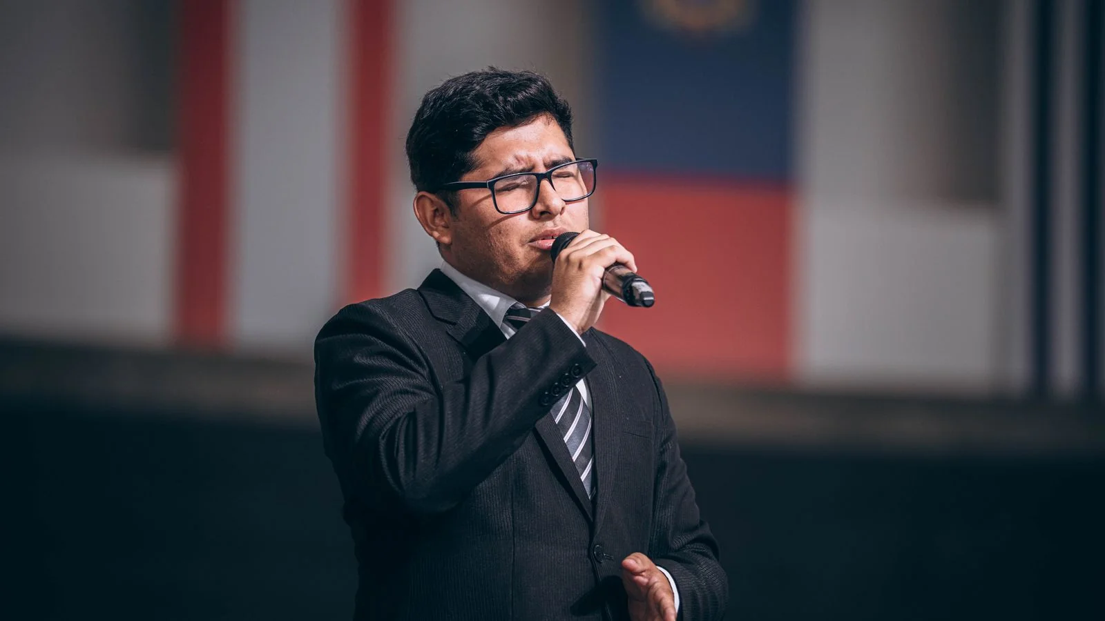 Man in a suit at a microphone in front of a row of flags, the public speaking that turns an operator into a source.