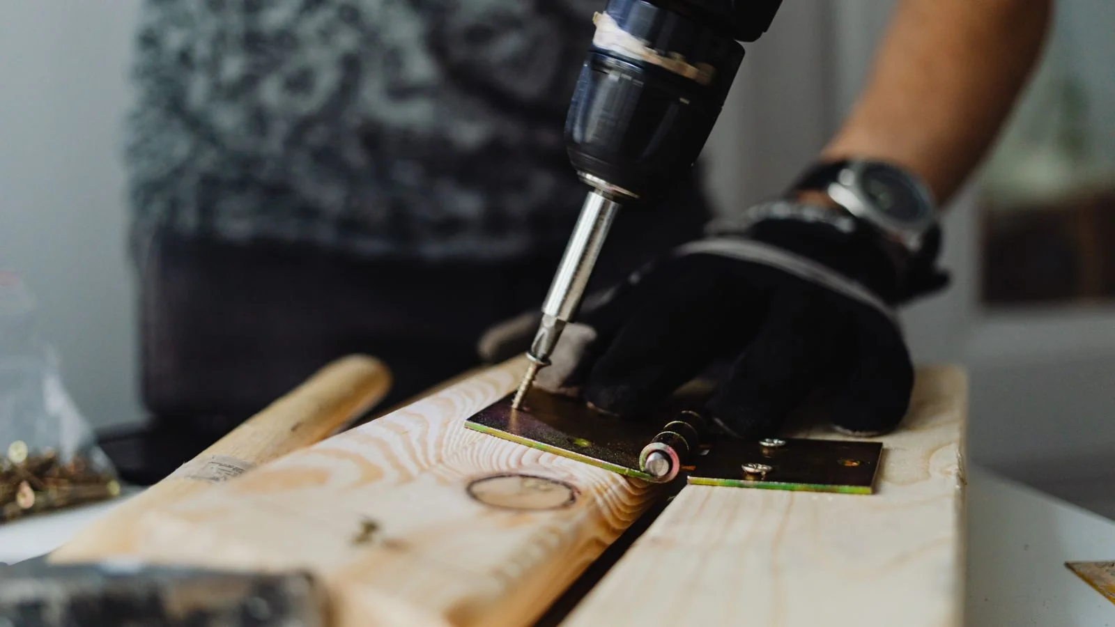 A handyman using a drill on a wooden plank indoors during a repair.
