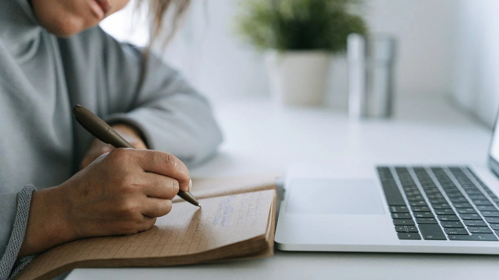 A person writing longhand in a notebook beside a closed laptop, the thinking step most content skips