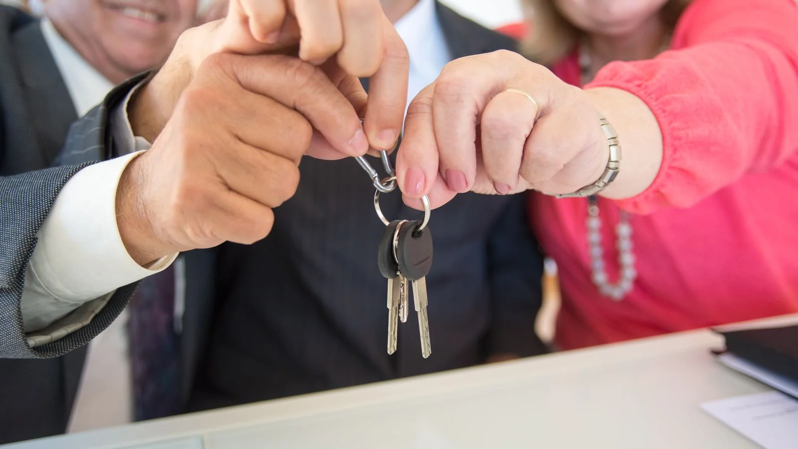 Loan officer handing house keys to a couple at a closing table, a story worth telling by name.