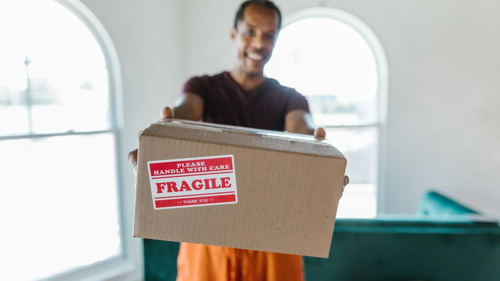 A person in a jacket carefully holding a cardboard box labeled fragile during a move.