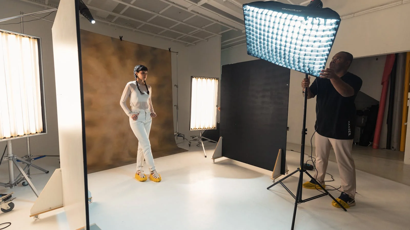 Photographer working with a model in a professional studio with controlled lighting and a posing stool