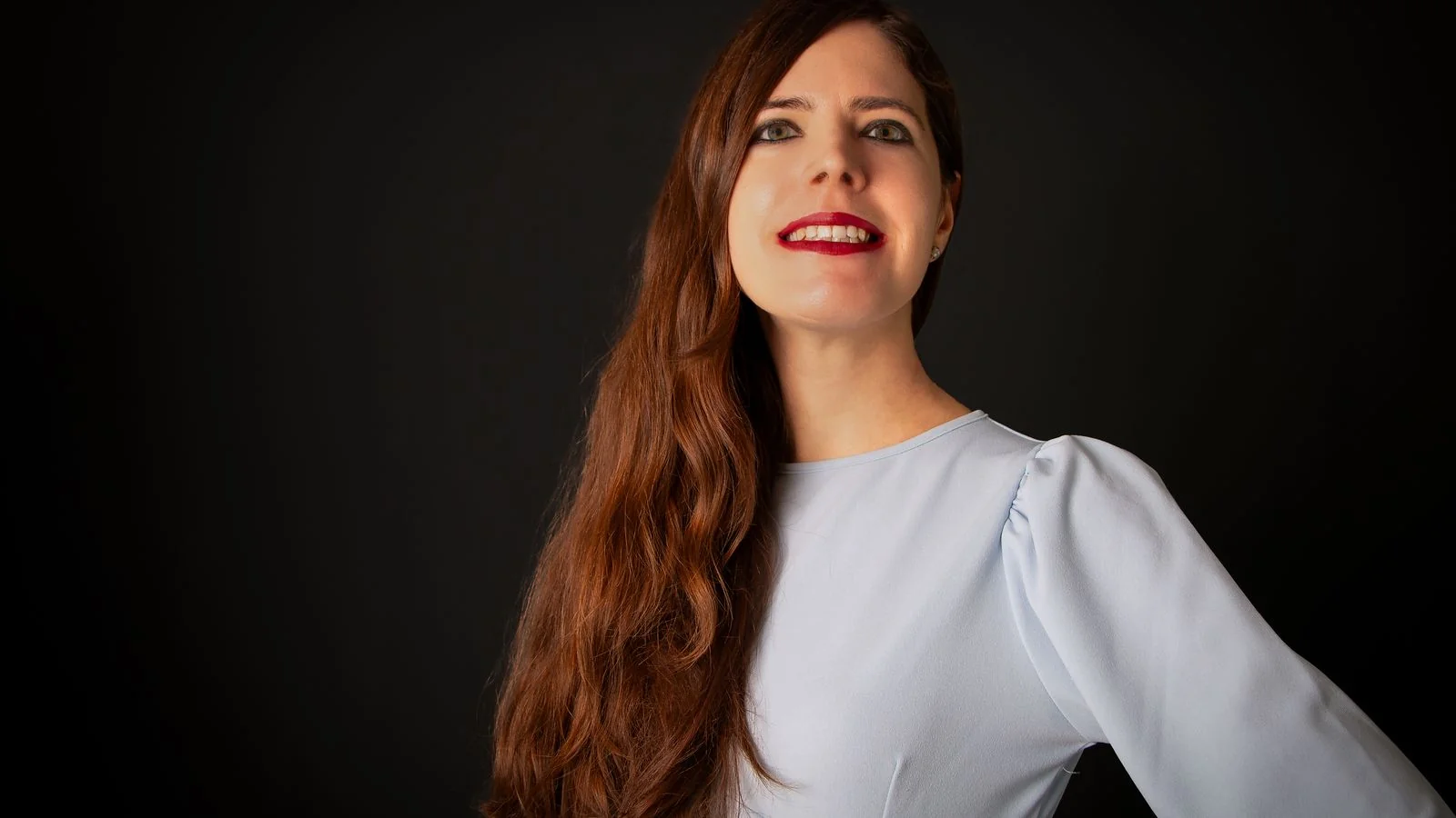 A confident studio portrait of a woman in a light dress against a dark background, projecting warmth and competence