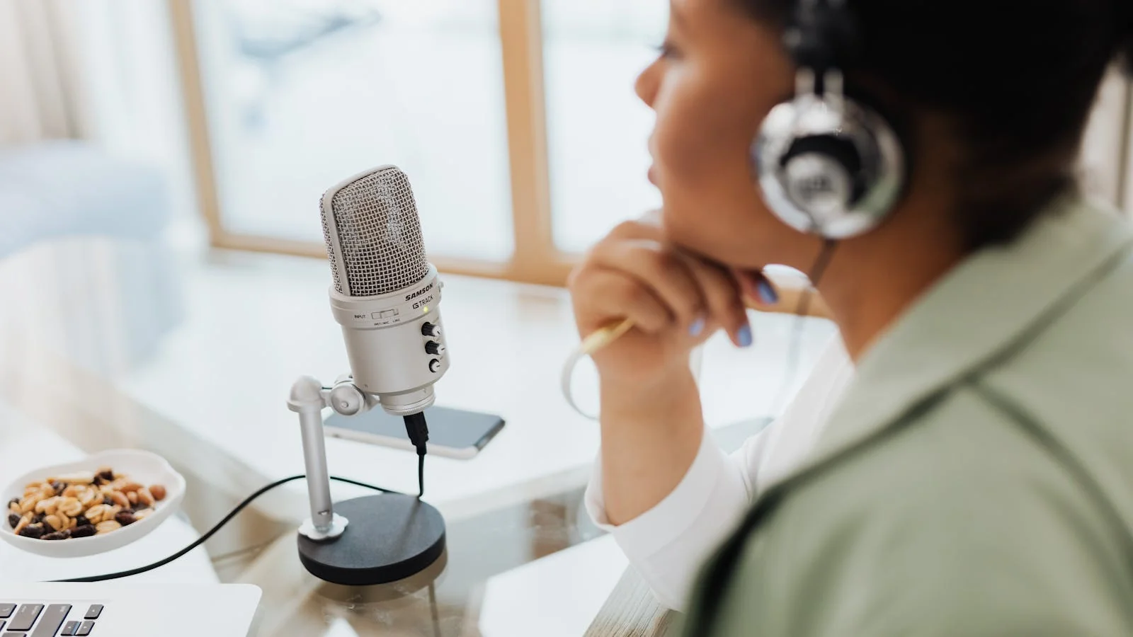 A guest with headphones at a desk, microphone and laptop in front of her, recording the kind of remote interview most podcasts run on in 2026.