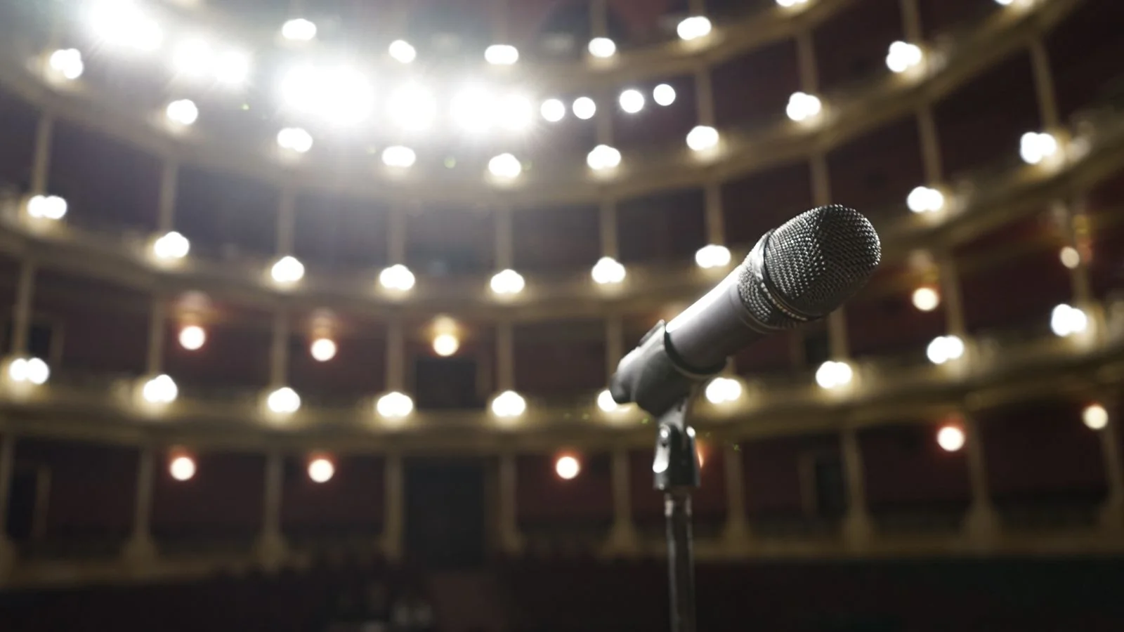 A microphone on a stand facing an empty lit theater, the stage a brand earns