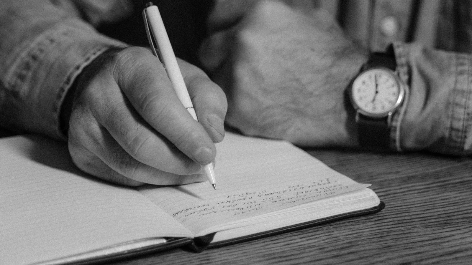 A person writing in a journal in low light, mining ordinary experience for the stories worth telling