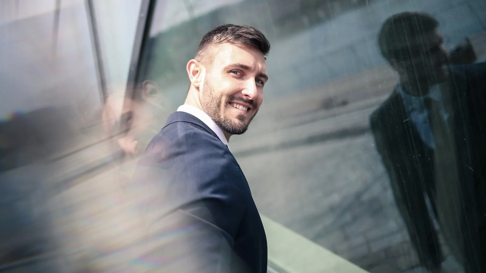 A bearded businessman smiles outdoors, projecting confidence and approachability.