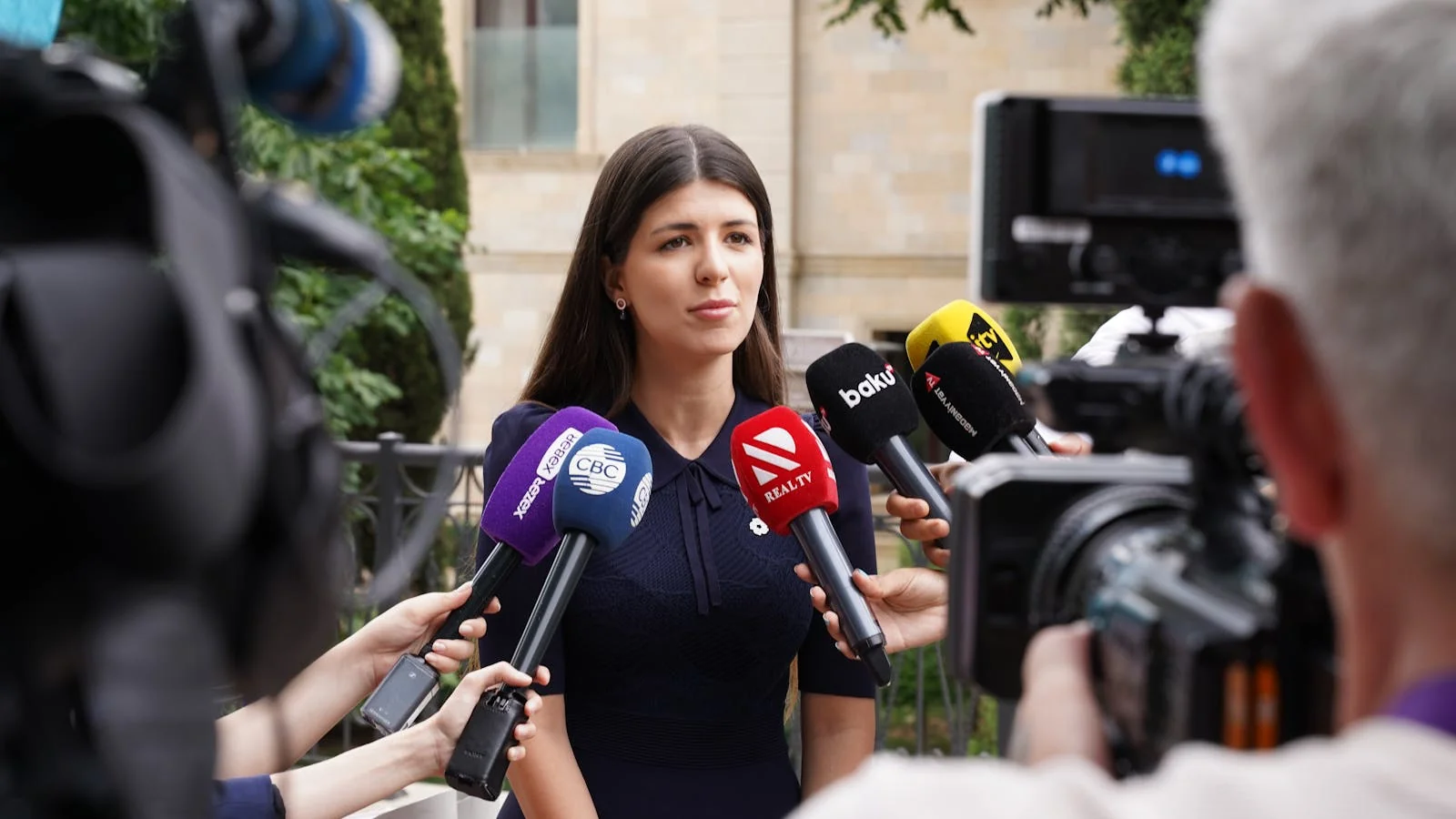 Female spokesperson giving a press interview with microphones and a journalist outside a venue immediately after a launch announcement