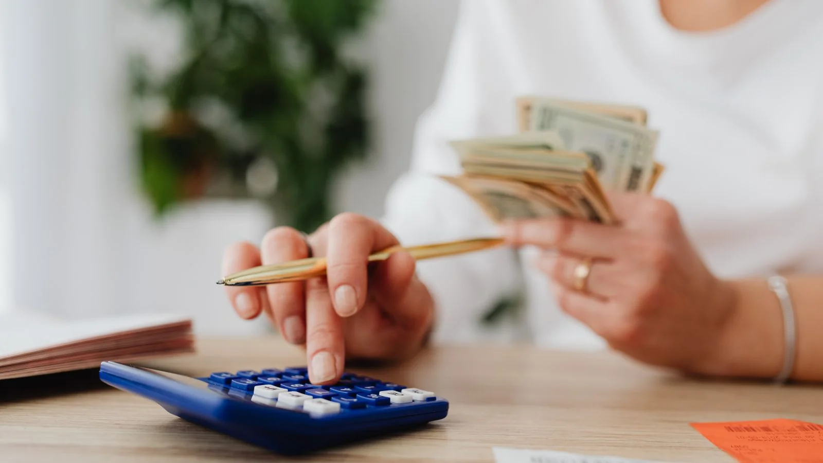 A person calculating finances with a calculator while holding cash at a desk