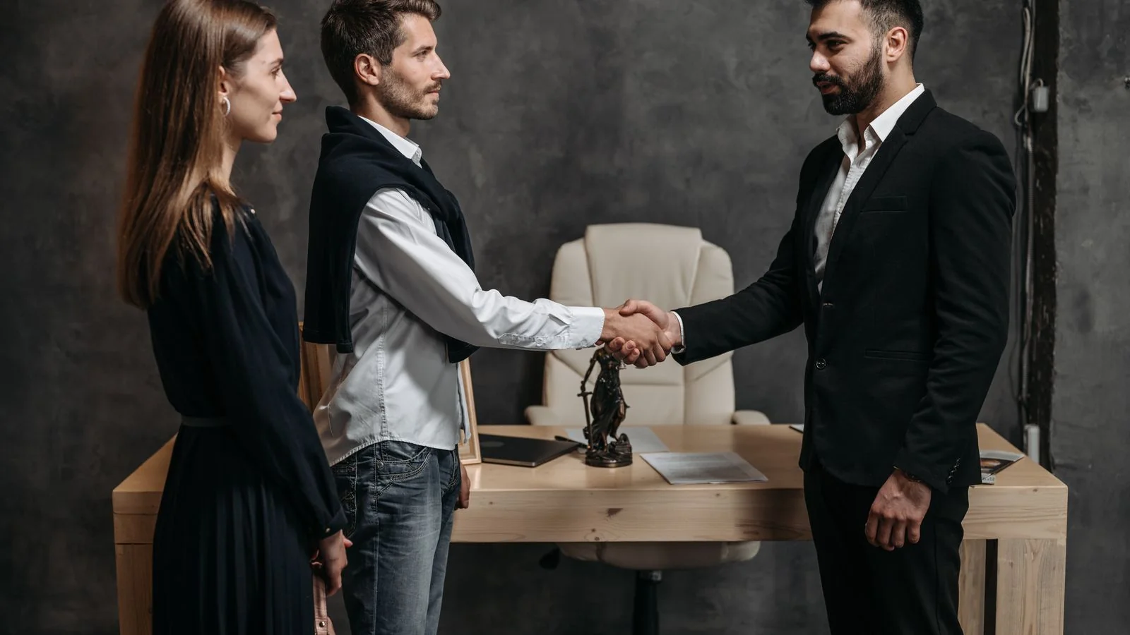 Three business professionals shaking hands across a table in a modern office after closing a deal