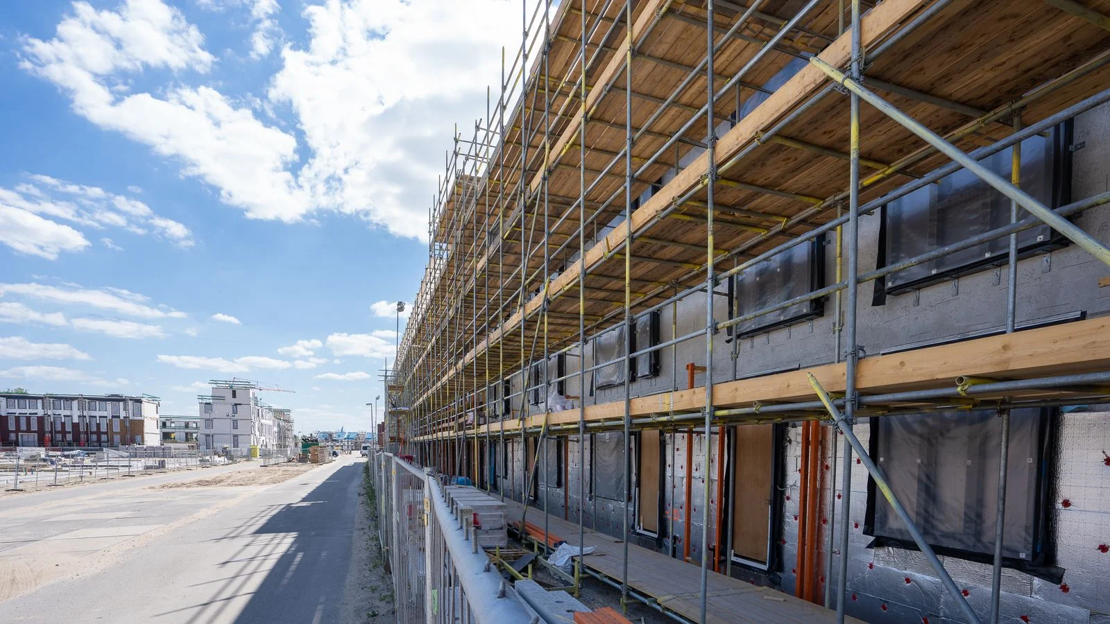 Scaffolding climbing a building facade at an urban construction site under a bright sky