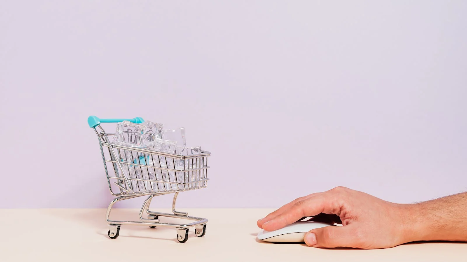 Hand on a mouse next to a miniature shopping cart, the moment of an ecommerce conversion