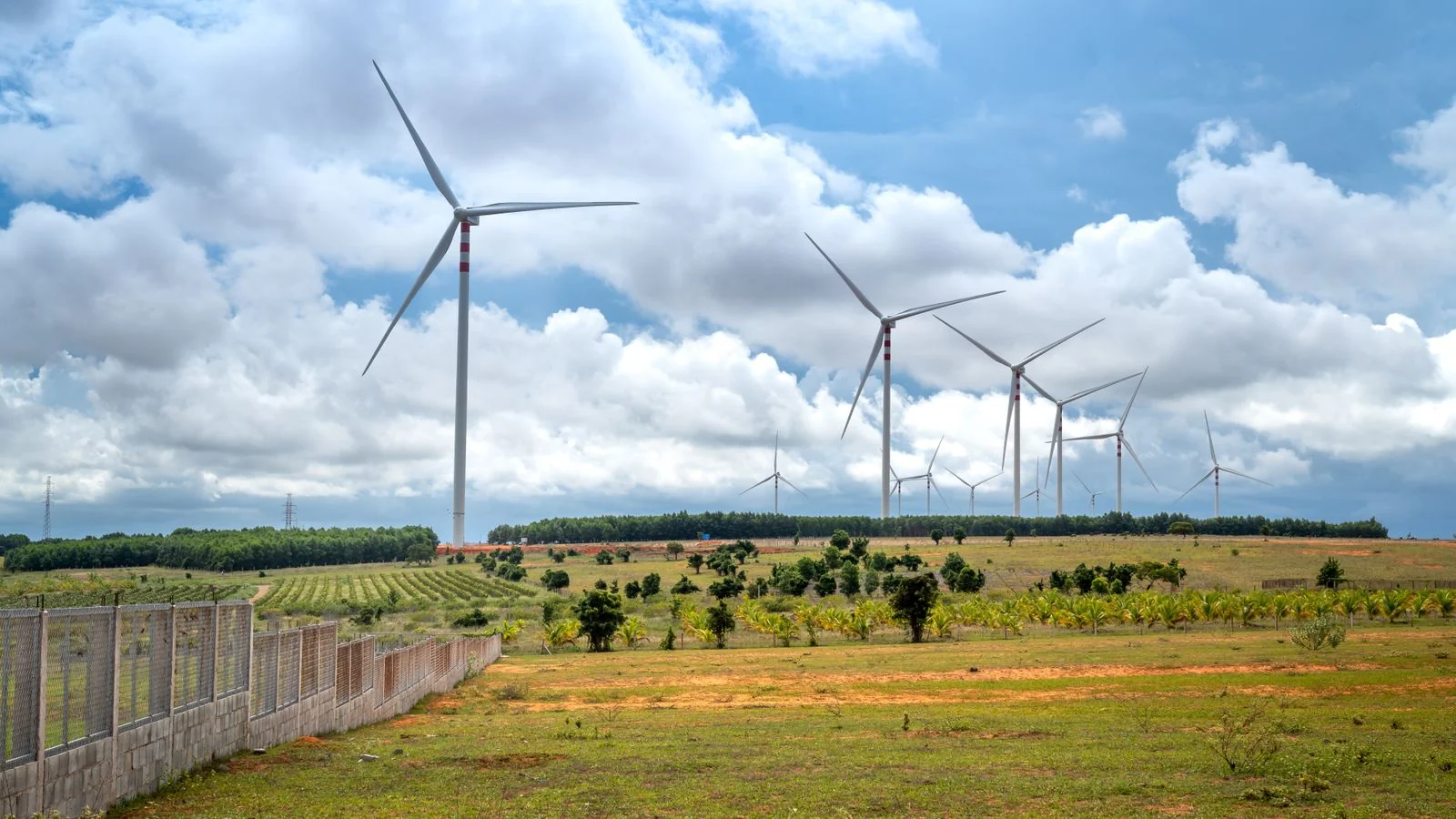 Wind turbines spinning across a green field under a bright sky