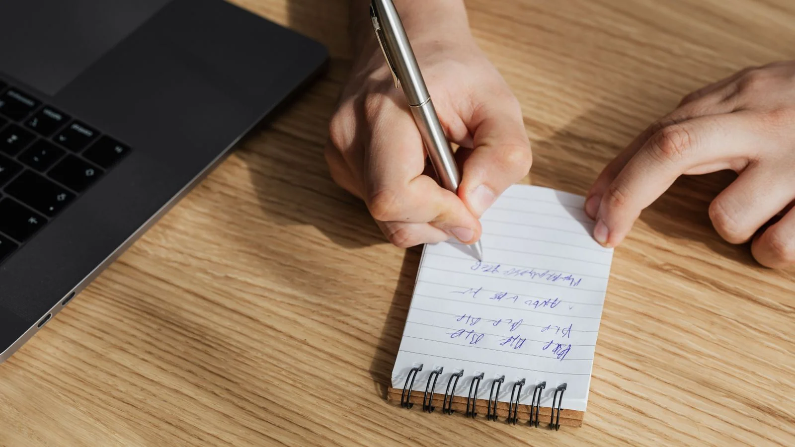 Person writing notes on a notepad at a desk, drafting the three lines that do the real work