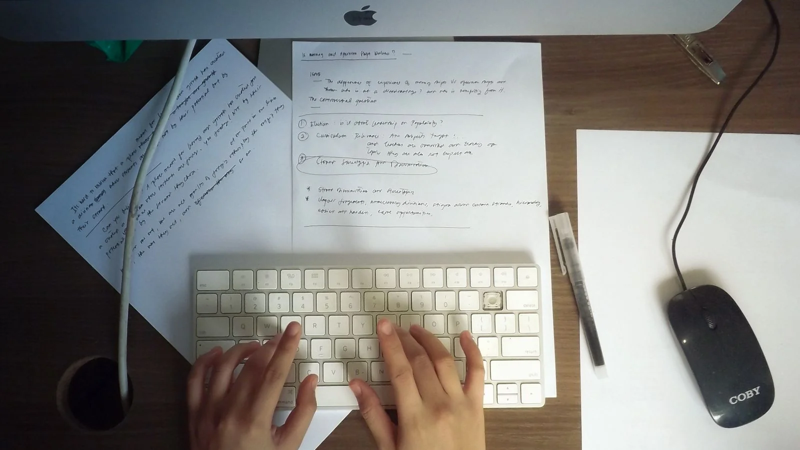 Hands typing on a keyboard at a desk with papers, drafting the full story a press release tells