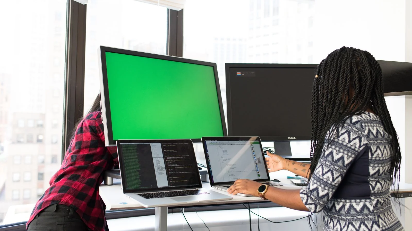 Two colleagues comparing analytics software on laptops and monitors in a bright office