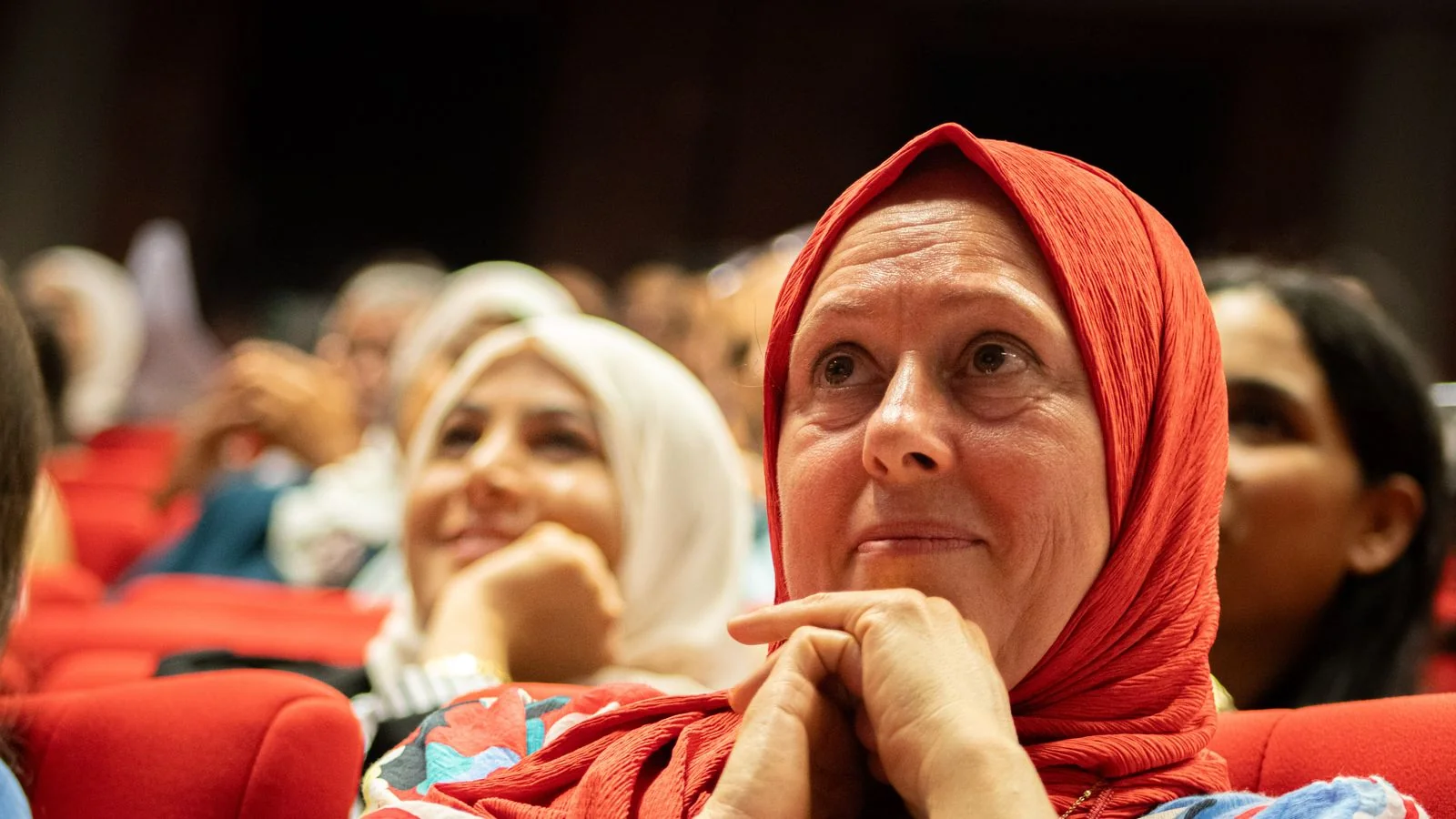 Audience members watching a speaker at an indoor cultural event, the view from the stage looking out