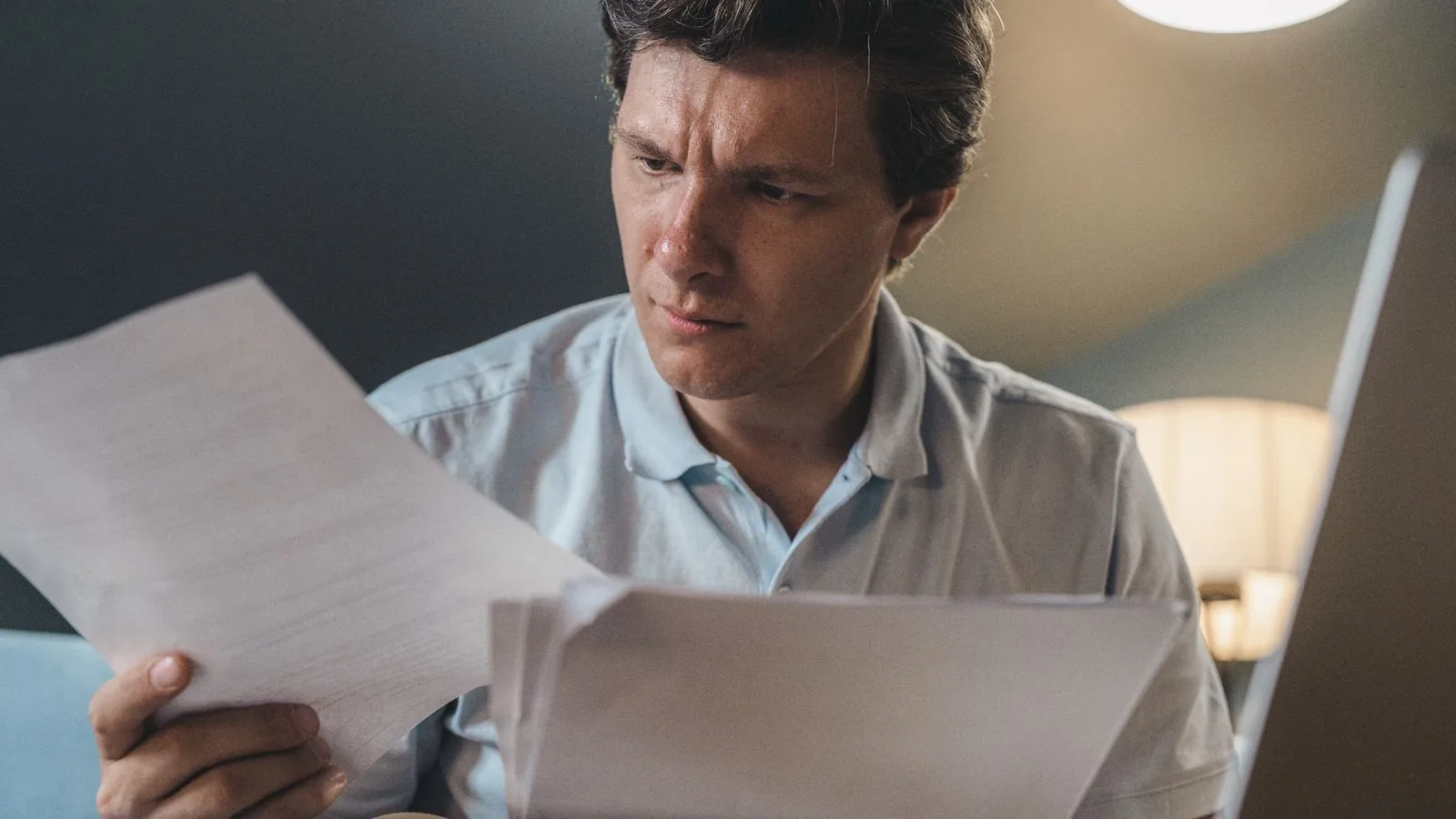 A man studying printed papers under warm light, the complaint file a clinic should be reviewing monthly