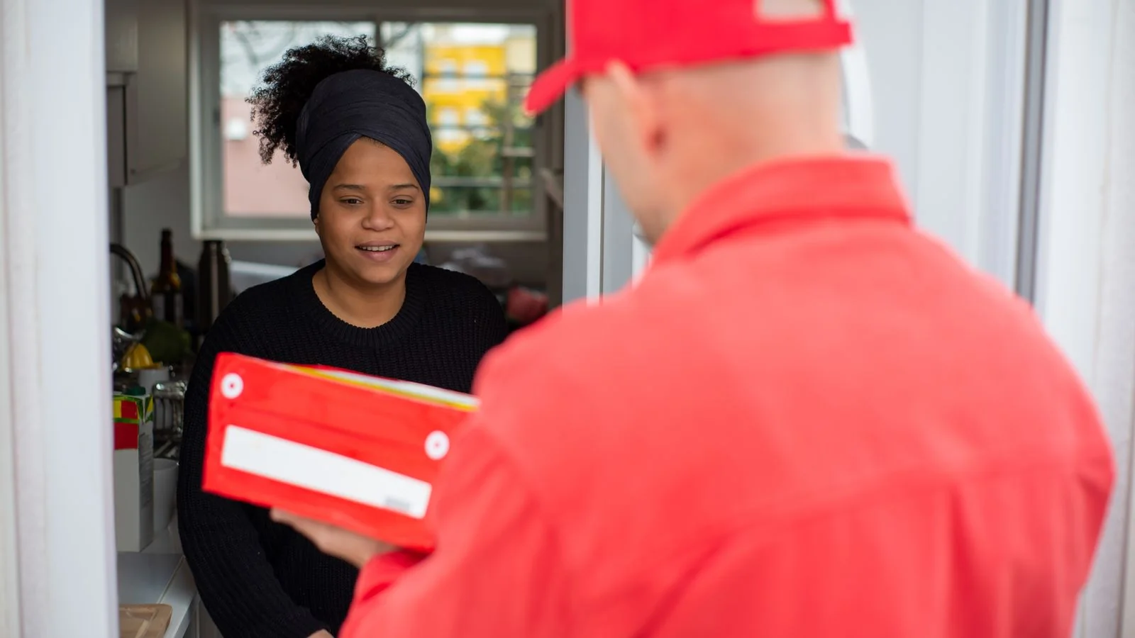 A courier hands a package to a smiling customer at a residential doorway.